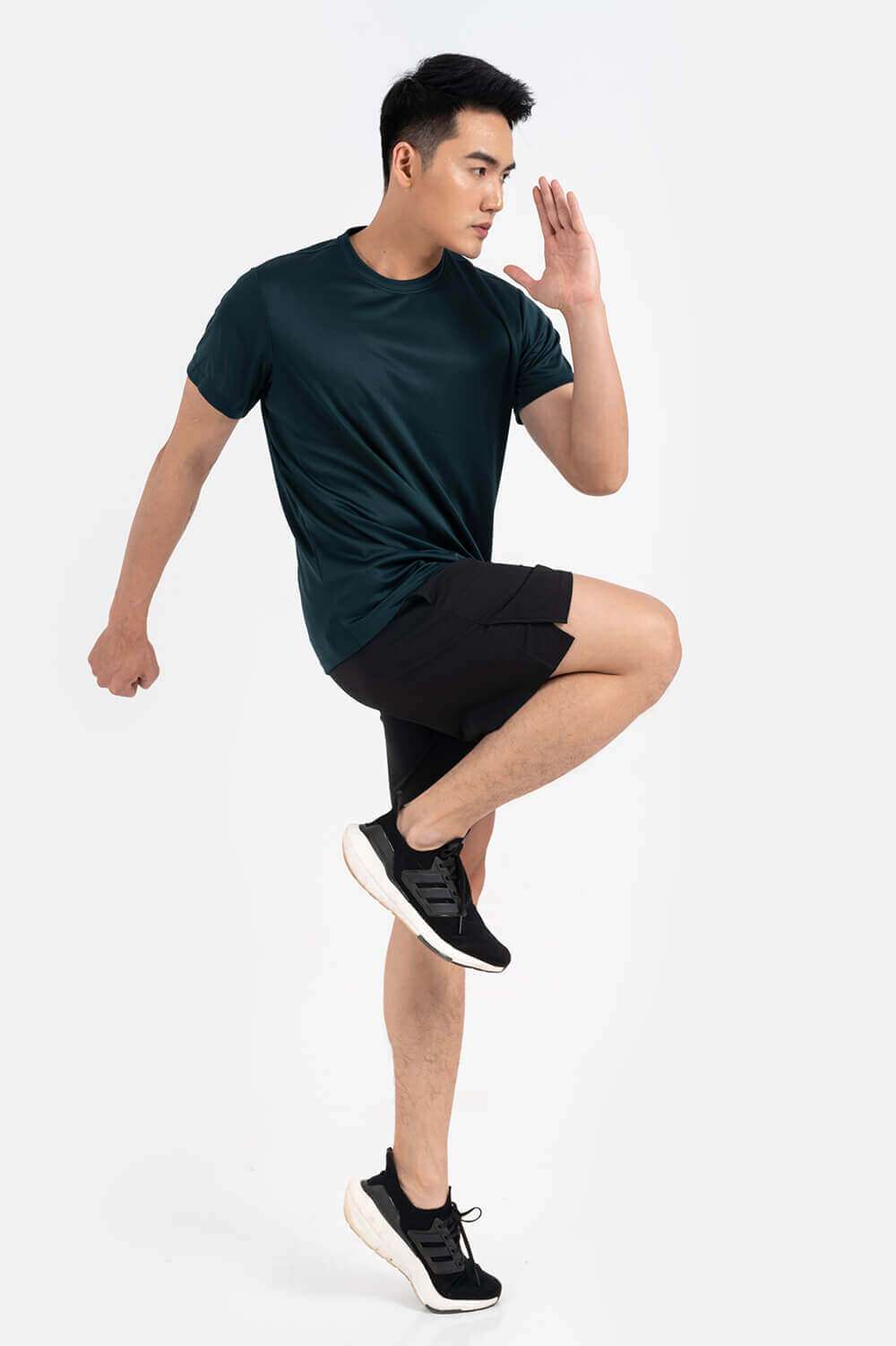 Người mẫu nam mặc áo thun thể thao màu xanh rêu và quần short đen trong tư thế vận động