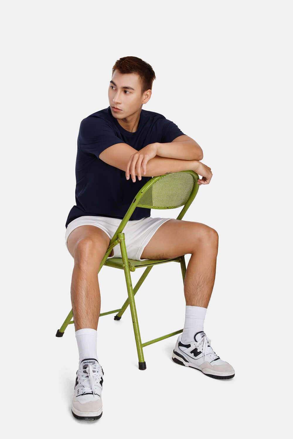 Người mẫu nam mặc áo thun cotton compact xanh navy và quần short trắng ngồi trên ghế