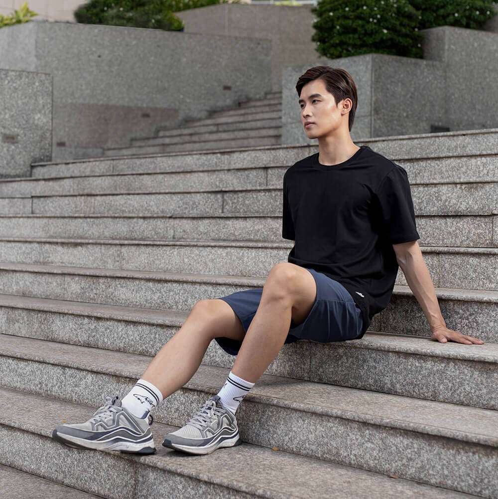 Người mẫu nam mặc áo thun cotton compact đen và quần short xám ngồi trên bậc thang